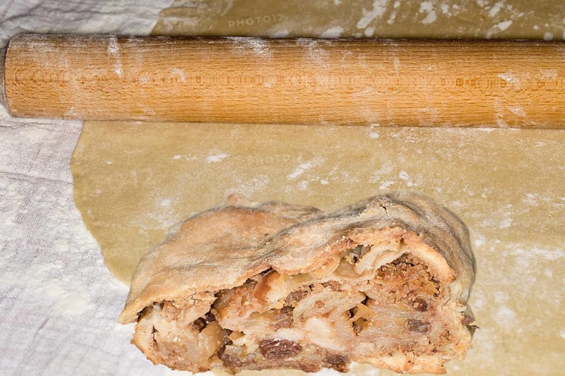 Rolling pin and a piece of apple strudel with sultanas lie on a strudel dough