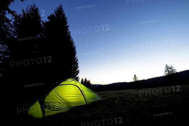 Illuminated green tent at the edge of the forest