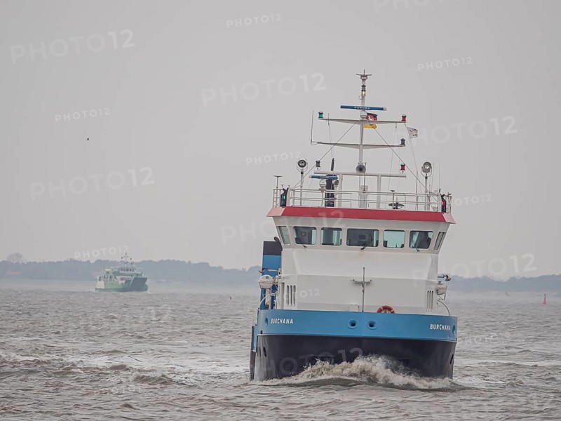 Supply ship Burchana with ferry Spiekeroog IV on the stormy North Sea entering the harbour