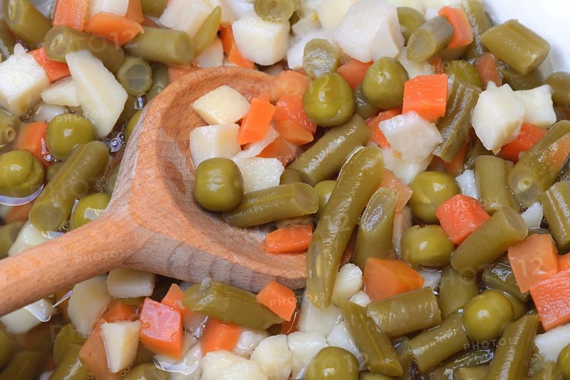 Ingredients for Russian salad in bowl and cooking spoon