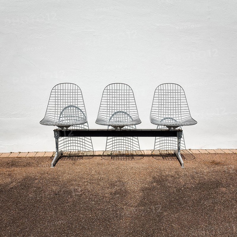 Three wire chairs in front of a white wall