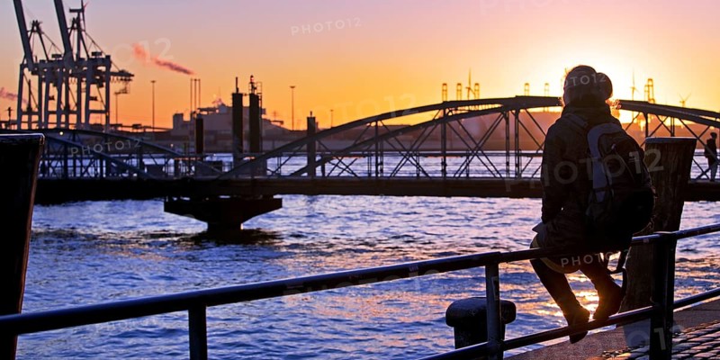 A woman sits on a railing at sunset on the Norderelbe in Altona