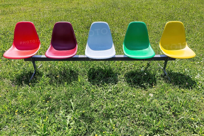 Five colourful plastic chairs in a meadow