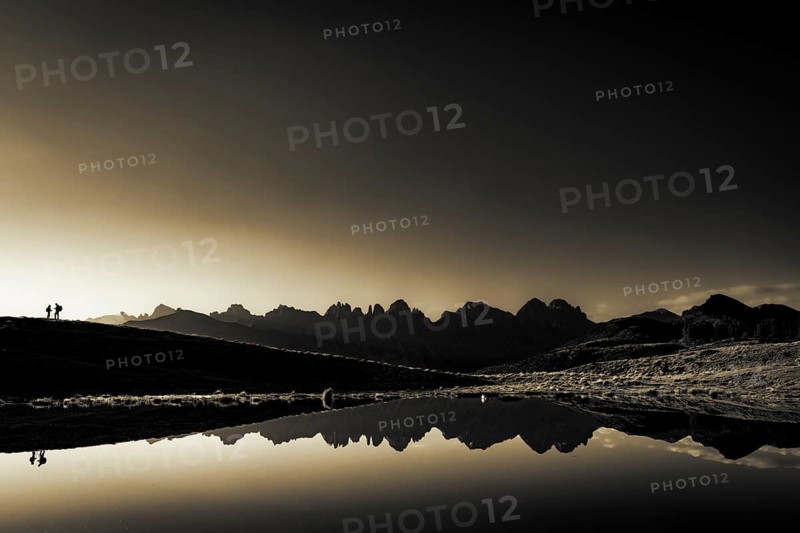 Salfainsee with reflection of the Kalkkoegel and mountaineers on mountain meadow at sunrise