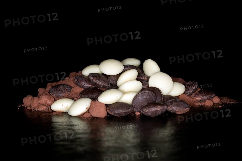 Dark and white couverture chocolate drops lying on cocoa powder