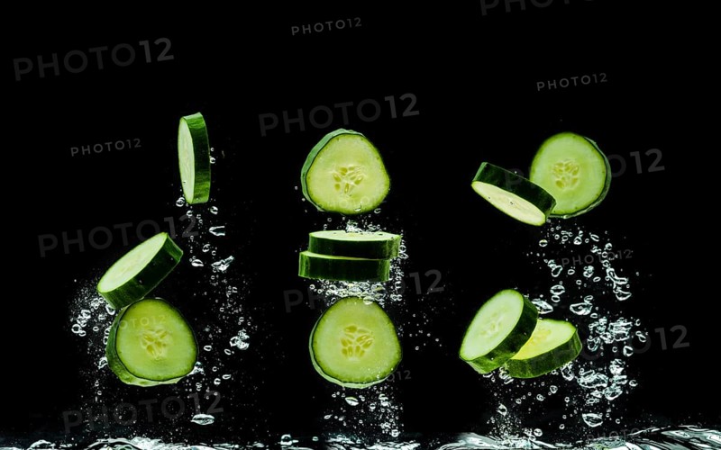 Sliced bio cucumber splashing water isolated on black background