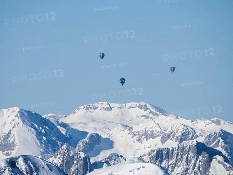 Hot air balloons flying over snow-covered Alpine peaks