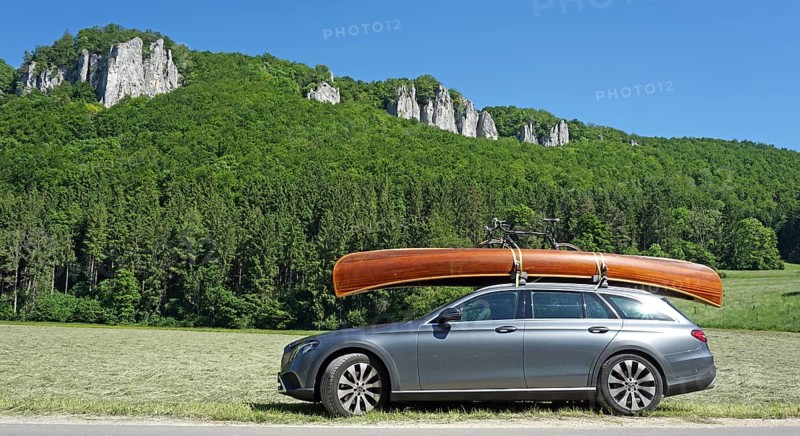 Mercedes with cedar wood canoe on roof in front of rocks in the Danube valley