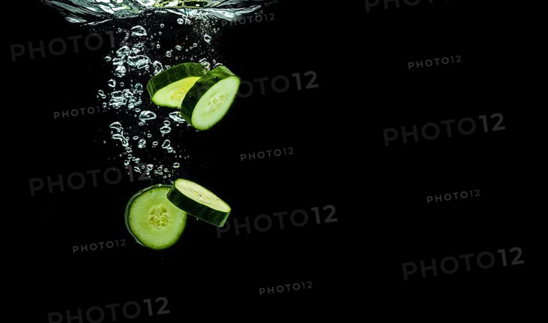 Sliced bio cucumber splashing water isolated on black background