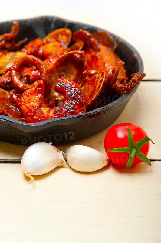 Fresh seafood stew prepared on an iron skillet ove white rustic wood table