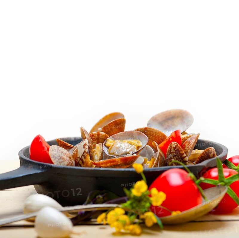 Fresh clams stewed on an iron skillet over wite rustic wood table