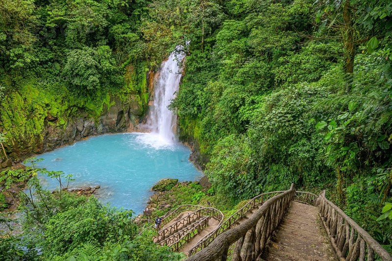 Many steps lead down to the waterfall with blue turquoise water of the Rio Celeste