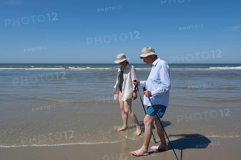 Elderly man accompanied by woman walking on the beach