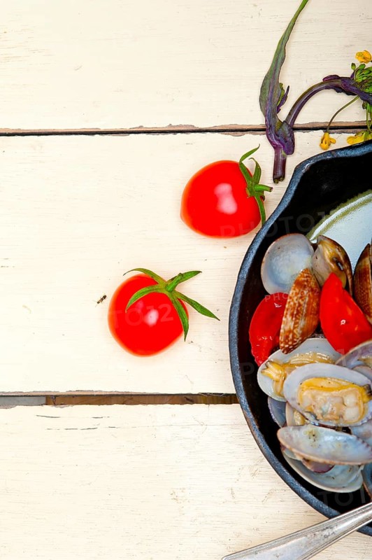 Fresh clams stewed on an iron skillet over wite rustic wood table