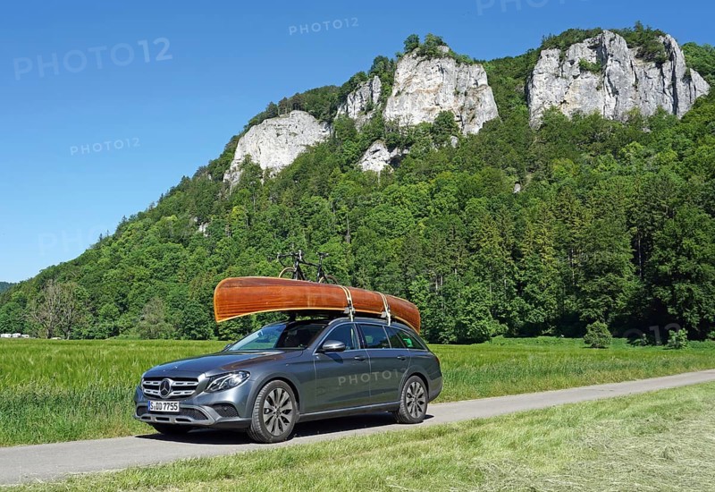 Mercedes with cedar wood canoe on roof in front of rocks in the Danube valley