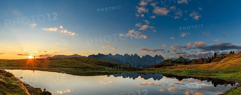Salfainsee with reflection of the Kalkkoegel and mountaineers on mountain meadow at sunrise