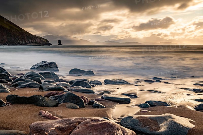 Sandy beach beach with stones on North Atlantic with rocky outcrop and cloudy sky