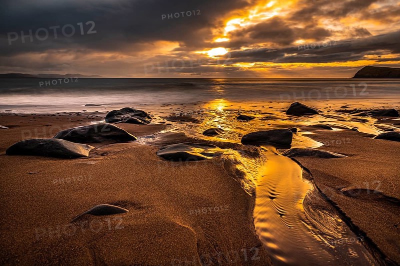 Sandy beach beach with stones on North Atlantic with rocky outcrop and cloudy sky at sunset