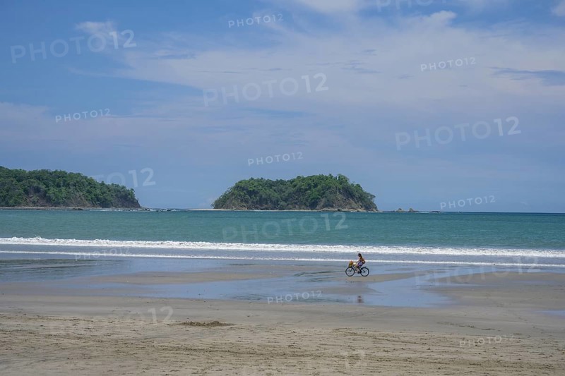 Woman riding a bicycle on the beach of Samara in the background Chora Island