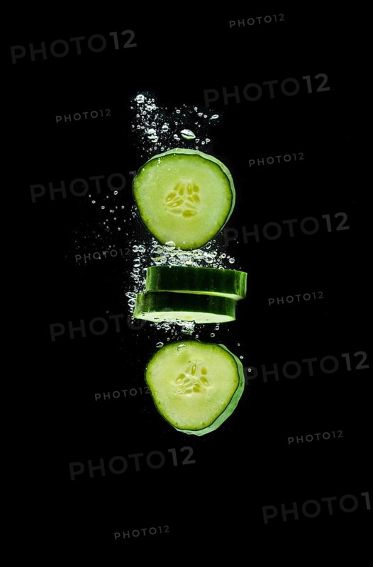 Sliced bio cucumber splashing water isolated on black background