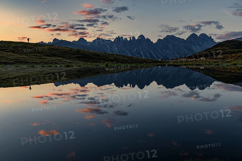 Salfainsee with reflection of the Kalkkoegel and mountaineers on mountain meadow at sunrise