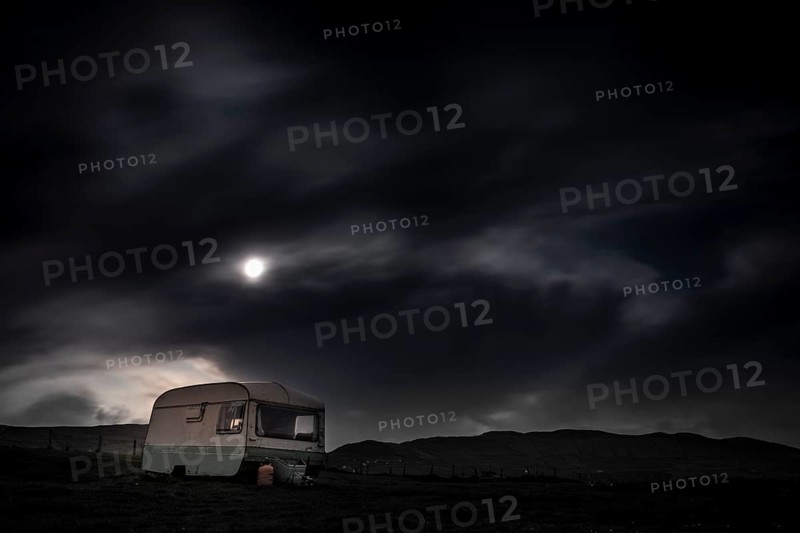 Old caravan in meadow under full moon