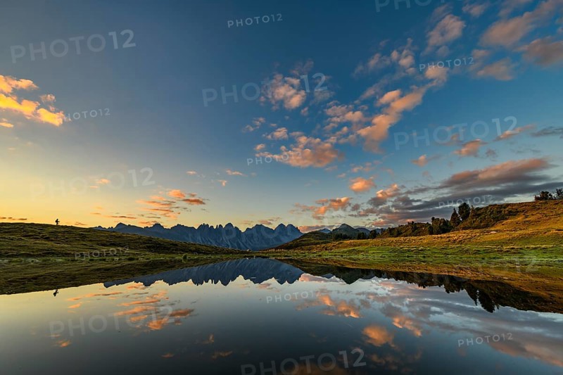 Salfainsee with reflection of the Kalkkoegel and mountaineers on mountain meadow at sunrise