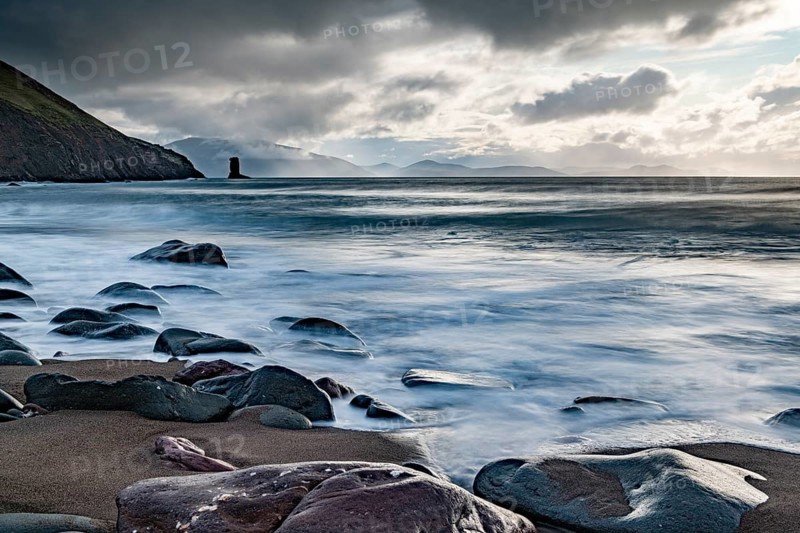 Sandy beach beach with stones on North Atlantic with rocky outcrop and cloudy sky