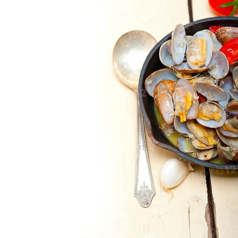 Fresh clams stewed on an iron skillet over wite rustic wood table