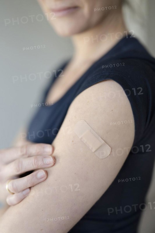 Arm of a woman with a plaster on her upper arm after vaccination