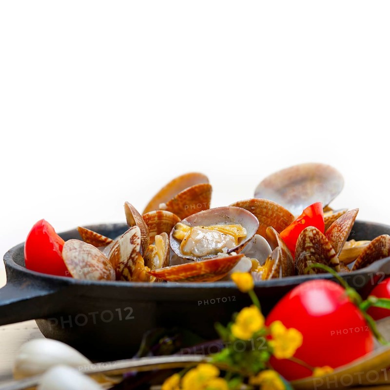 Fresh clams stewed on an iron skillet over wite rustic wood table
