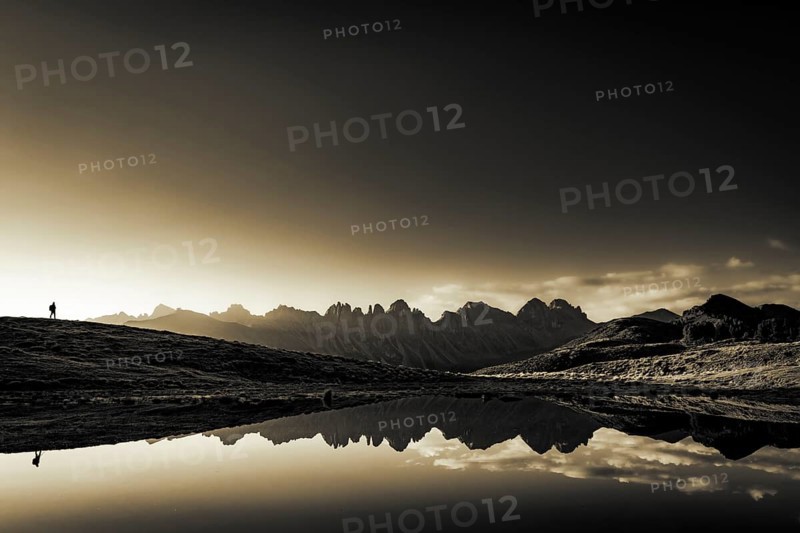 Salfainsee with reflection of the Kalkkoegel and mountaineers on mountain meadow at sunrise