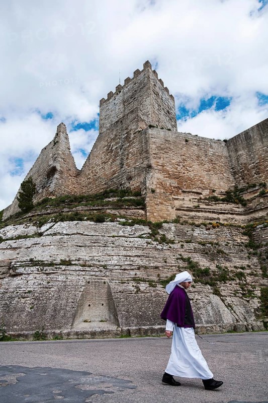 A young men dressed in the attire of one of the numerous brotherhoods of Enna walking in front of the castle of Enna