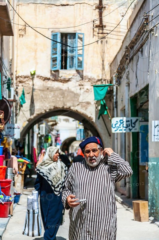 An elderly man in traditional attire walking through the streets of the old town of Tripoli
