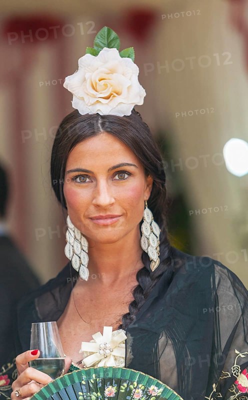 Portrait of a beautiful young woman in traditional attire and sherry glass in hand during the week-long Feria de Abril in Seville