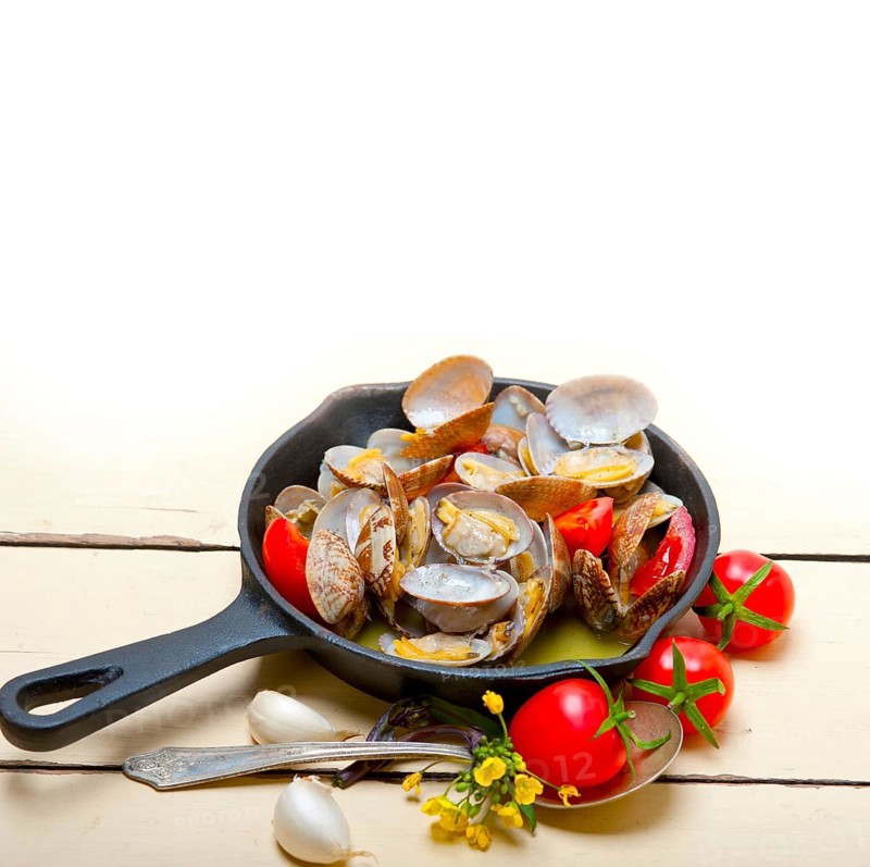 Fresh clams stewed on an iron skillet over wite rustic wood table