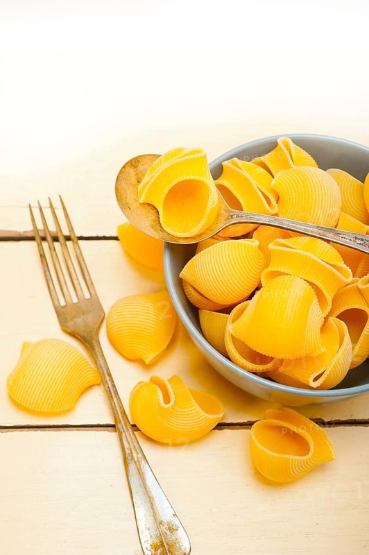 Raw Italian snail lumaconi pasta on a blue bowl over rustic table macro