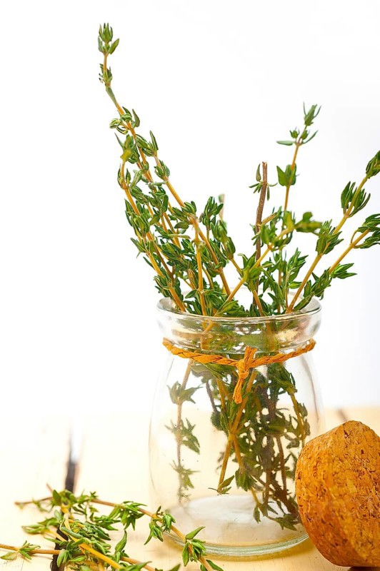 Fresh thyme on a glass jar over a white wood rustic table