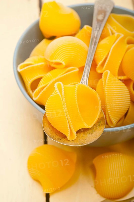 Raw Italian snail lumaconi pasta on a blue bowl over rustic table macro