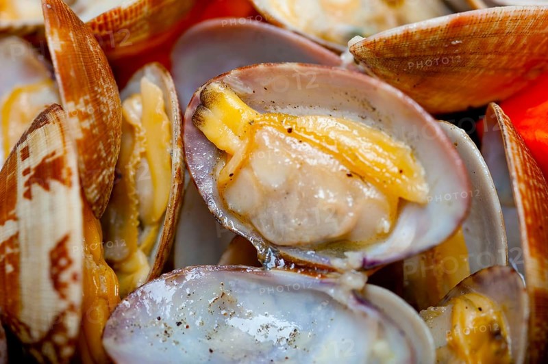 Fresh clams stewed on an iron skillet over wite rustic wood table
