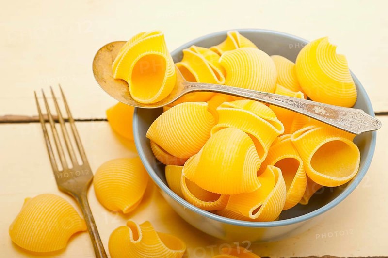 Raw Italian snail lumaconi pasta on a blue bowl over rustic table macro