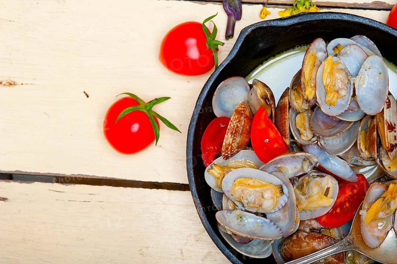 Fresh clams stewed on an iron skillet over wite rustic wood table