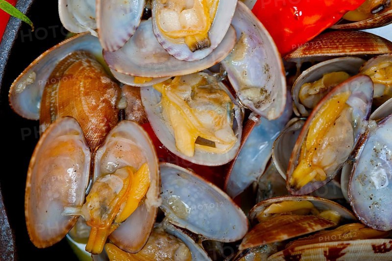 Fresh clams stewed on an iron skillet over wite rustic wood table