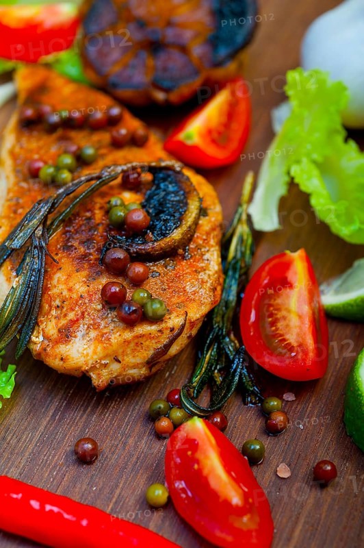 Wood fired hoven cooked chicken breast on wood board with herbs spices and vegetables