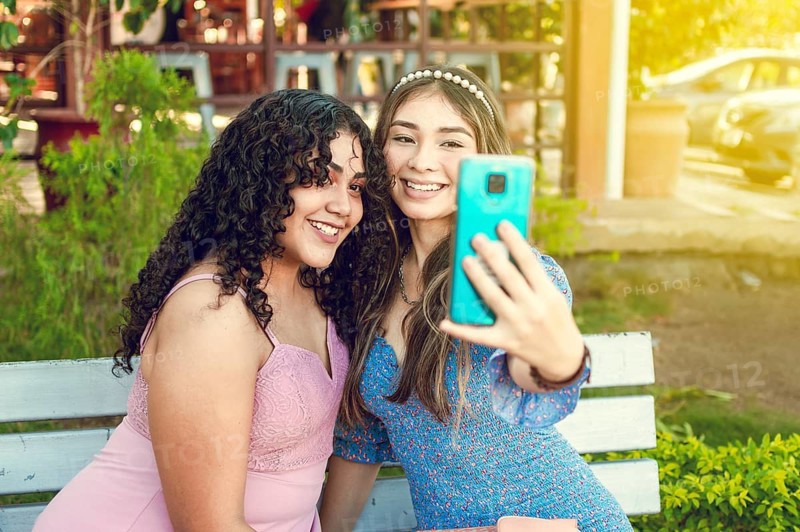 Two pretty girls sitting on a bench taking a selfie