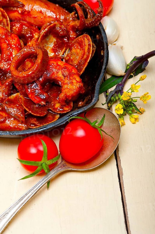 Fresh seafood stew prepared on an iron skillet ove white rustic wood table