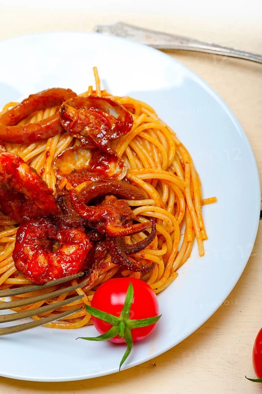 Italian seafood spaghetti pasta on red tomato sauce over white rustic wood table