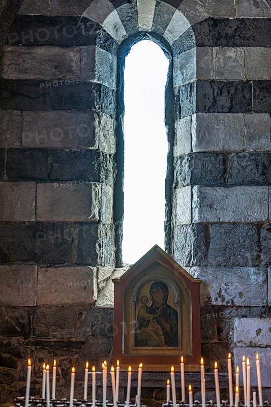 Burning candles in front of an image of the Virgin Mary in front of an open window of the church of San Pietro