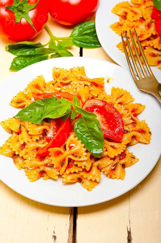 Italian pasta farfalle butterfly bow-tie with tomato basil sauce over white rustic wood table