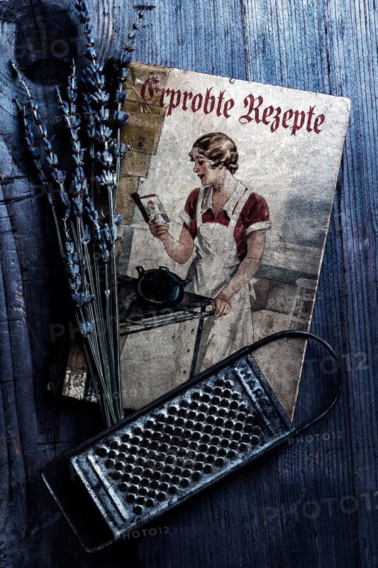 Old cookbook with lavender and kitchen grater on rustic background